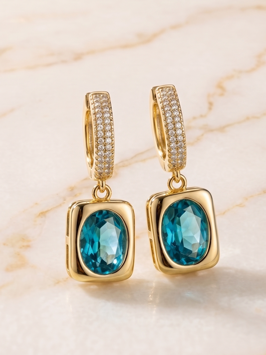 Gold earrings with blue gemstones on a marble background