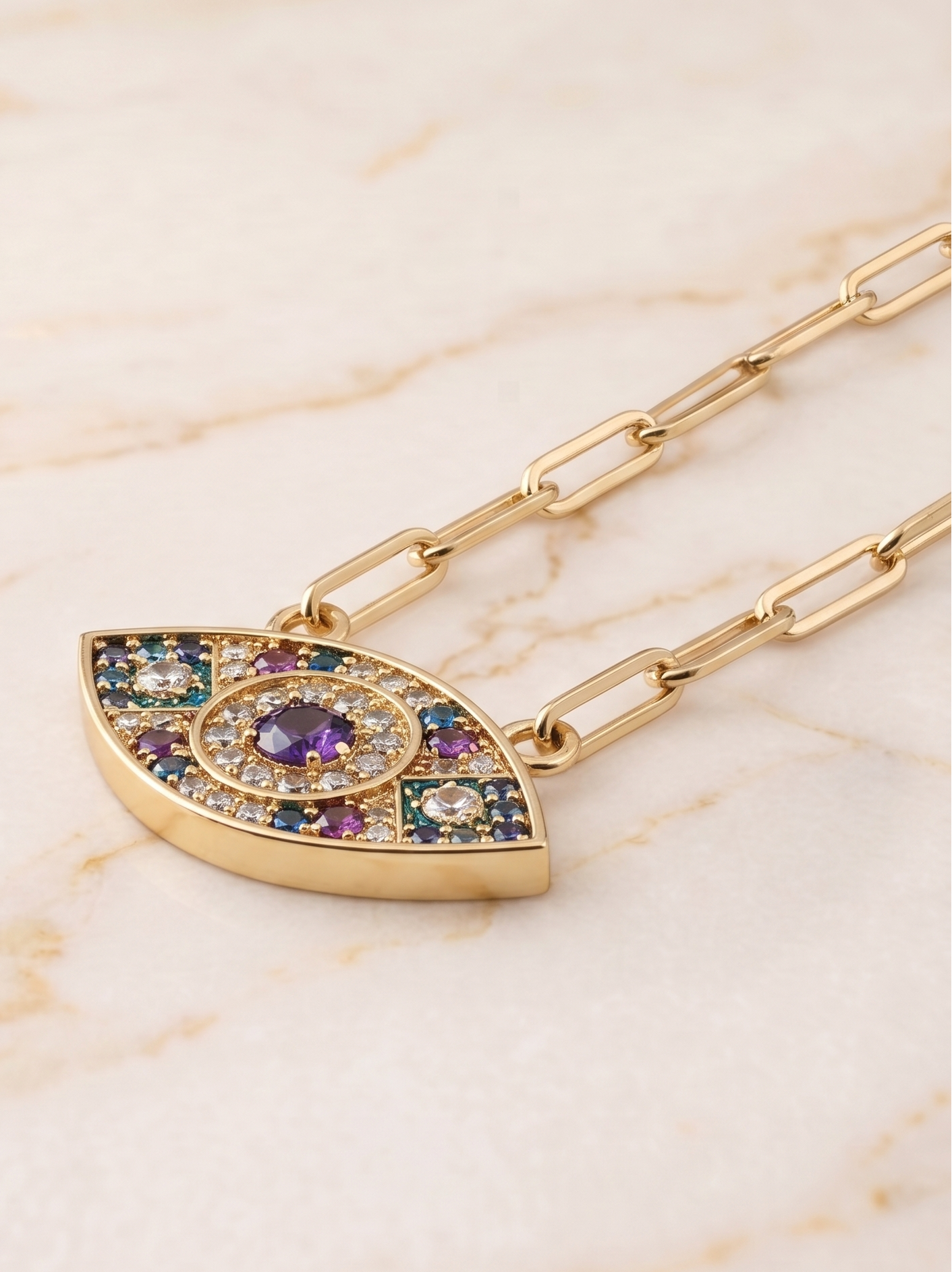 Gold necklace with a colorful eye-shaped pendant on a marble background