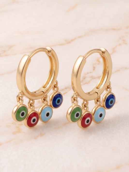 Gold hoop earrings with colorful evil eye charms on a beige marble background