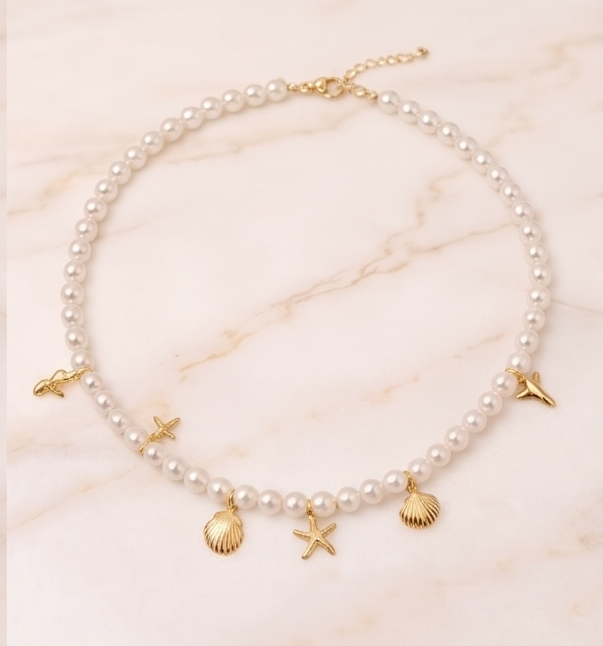 Pearl necklace with gold charms on a marble surface